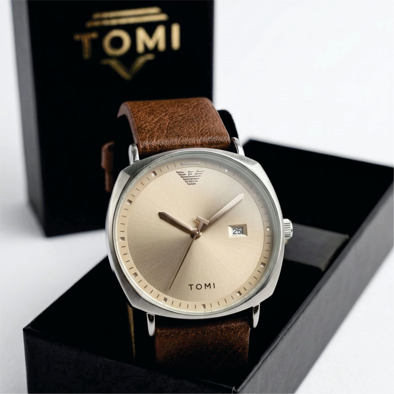 Watch with brown leather strap and gold face on a black box with 'TOMI' branding.